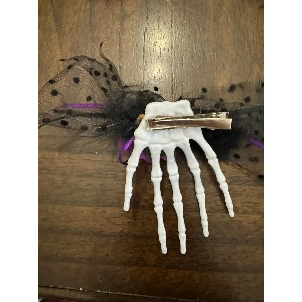Purple rose hair clip with black netting and purple ribbon on a skeleton hand